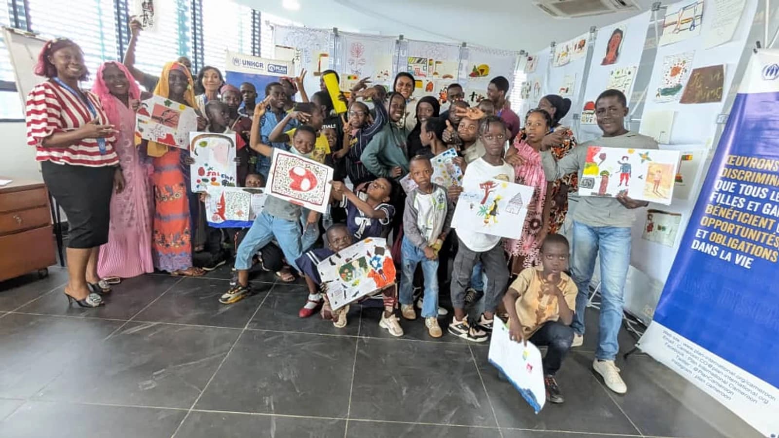 Enfants bénéficiaires brandissant leurs œuvres lors de l'atelier Plan International & UNHCR